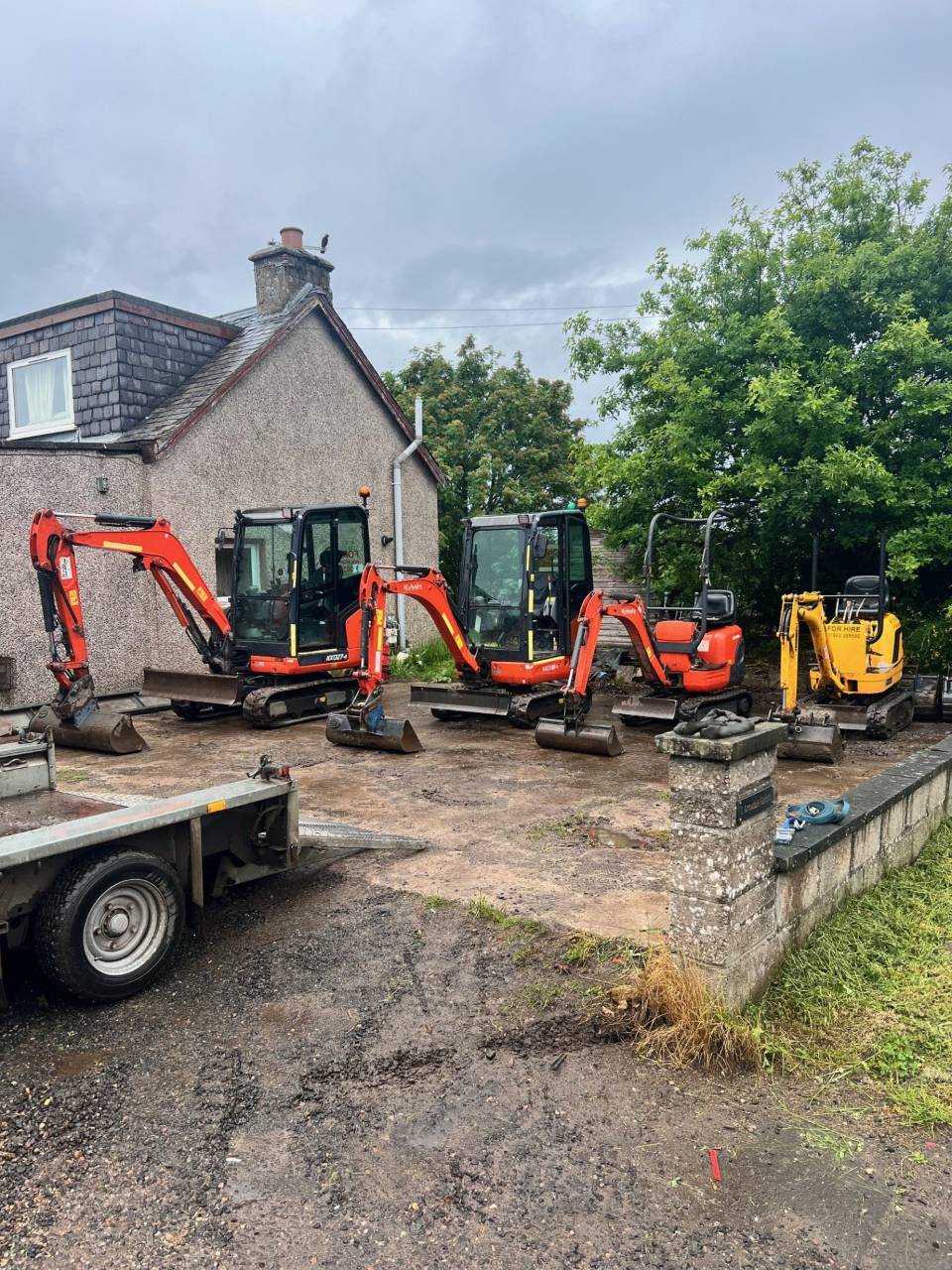 Three excavators parked outside a rural house.