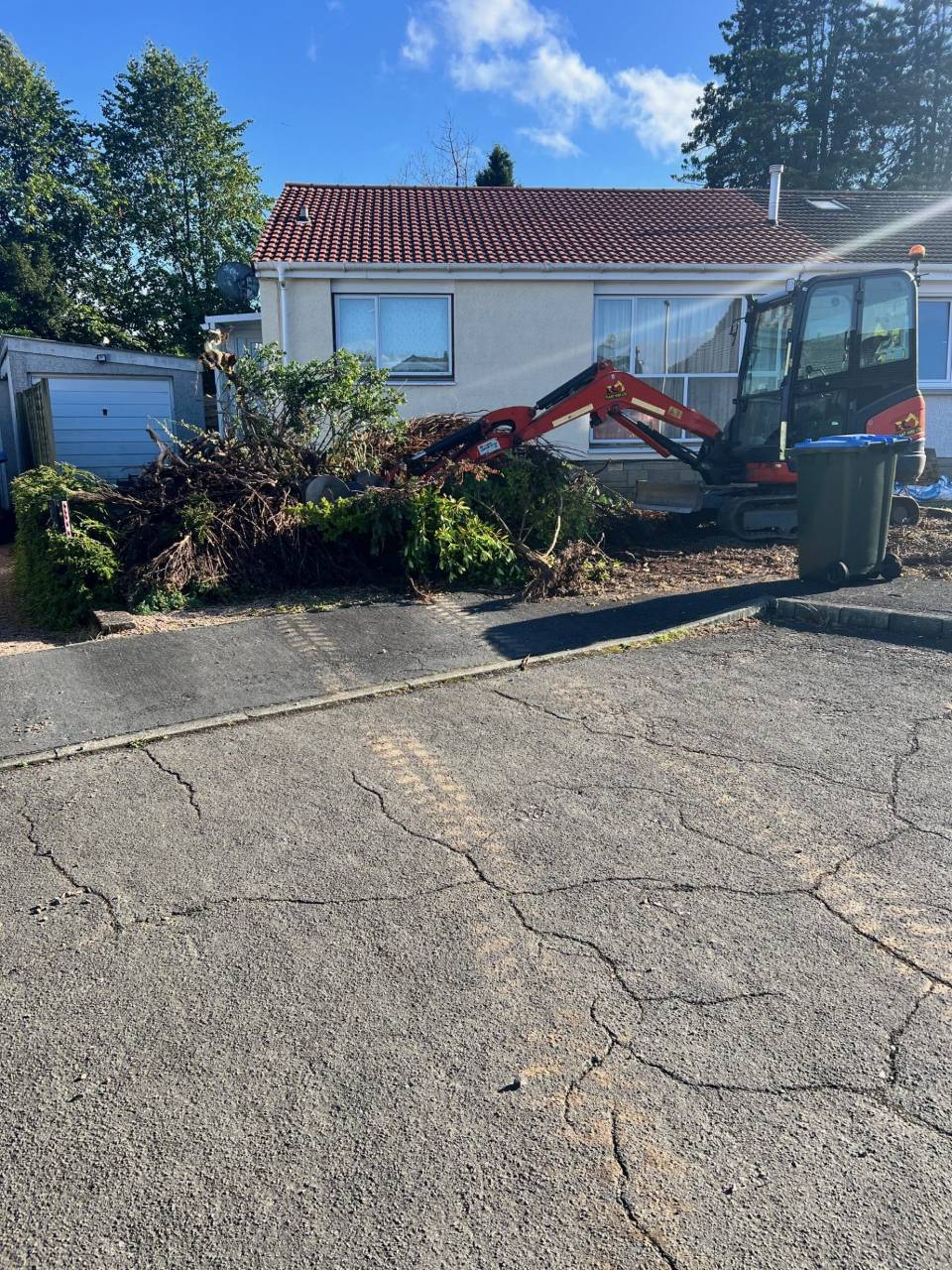 Mini-excavator clearing bushes outside a home.