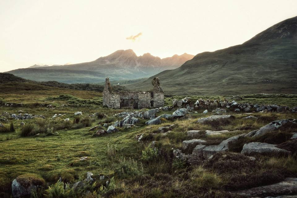 Abandoned stone cottage in green hilly landscape.