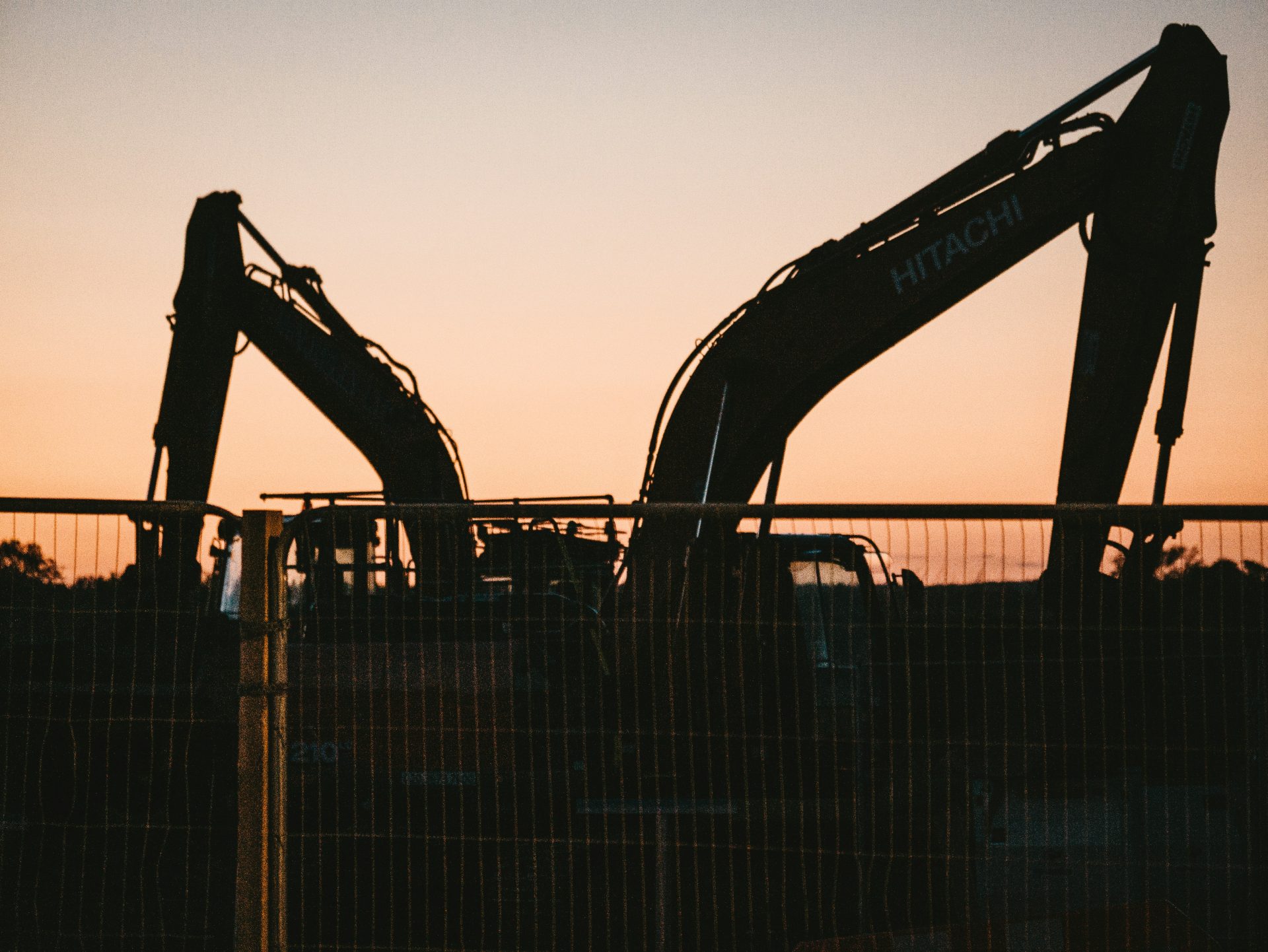 Silhouetted excavators against a sunset backdrop.