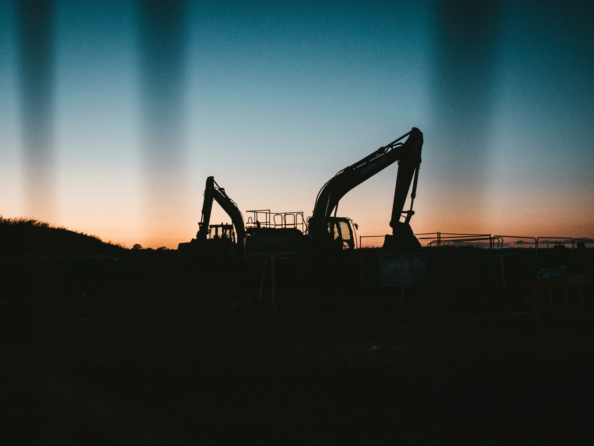 Silhouetted excavators working against twilight sky.